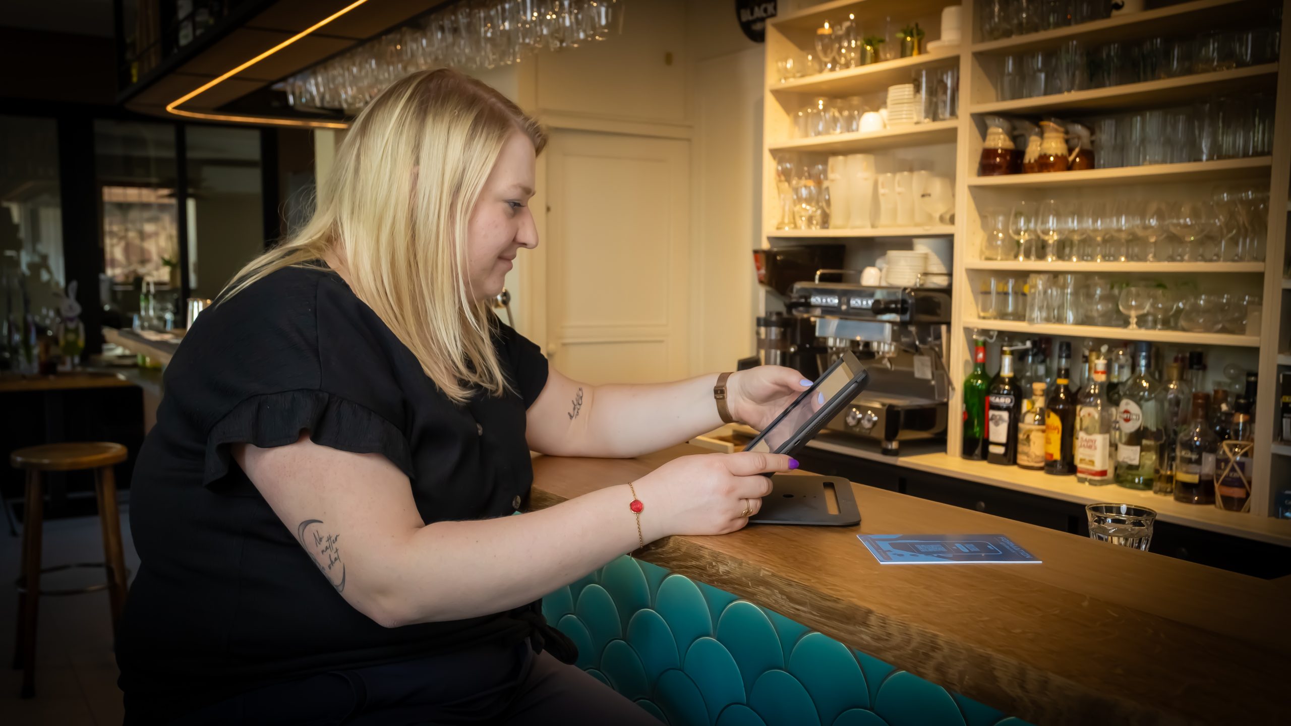 Une femme cheffe d'un restaurant en train de suivre la formation en ligne de gestion de bar directement dans son établissement à l'aide d'une tablette : Devenir Barman