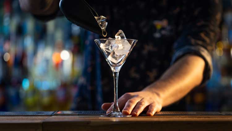 VERS DANS UN VERRE A MARTINI AVEC DES GLACONS AVEC 2 MAIN D'UN BARMAN ALSACIEN